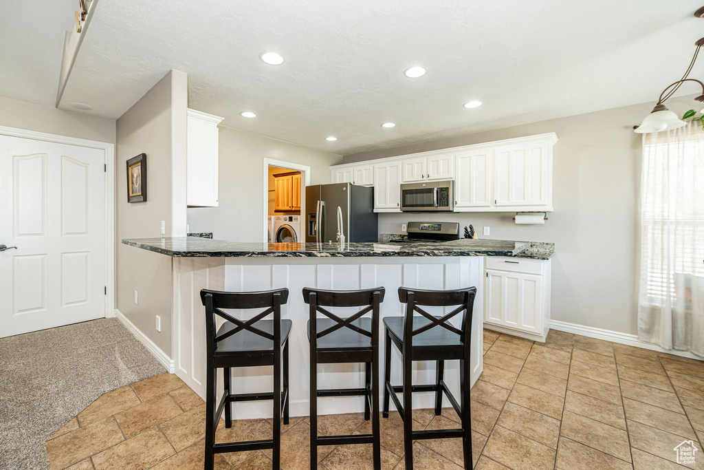 Kitchen featuring stainless steel appliances, washer / clothes dryer, a breakfast bar area, white cabinetry, and recessed lighting