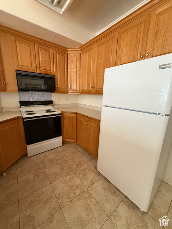 Kitchen featuring white appliances, light countertops, light tile patterned floors, and brown cabinets