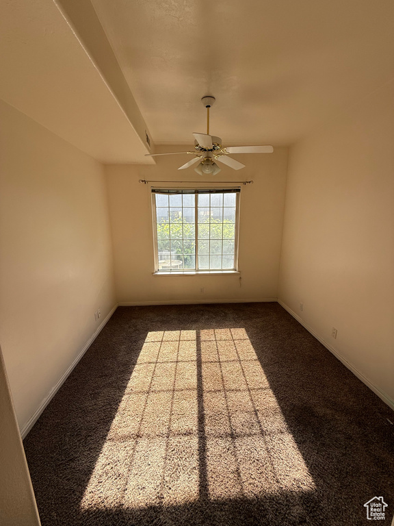 Empty room featuring a ceiling fan and dark colored carpet
