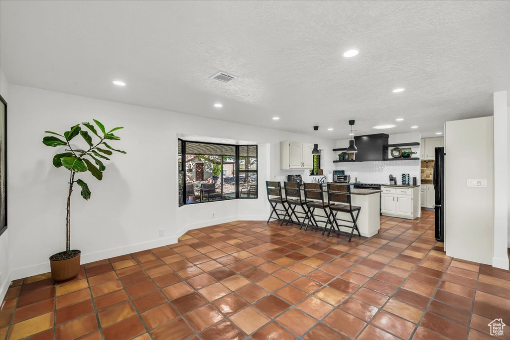 Kitchen with a kitchen breakfast bar, recessed lighting, freestanding refrigerator, white cabinets, and a textured ceiling