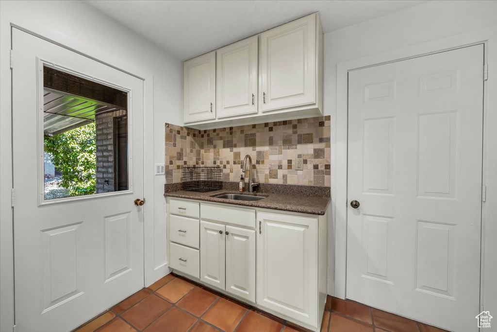 Kitchen with tasteful backsplash, dark tile patterned floors, and white cabinets
