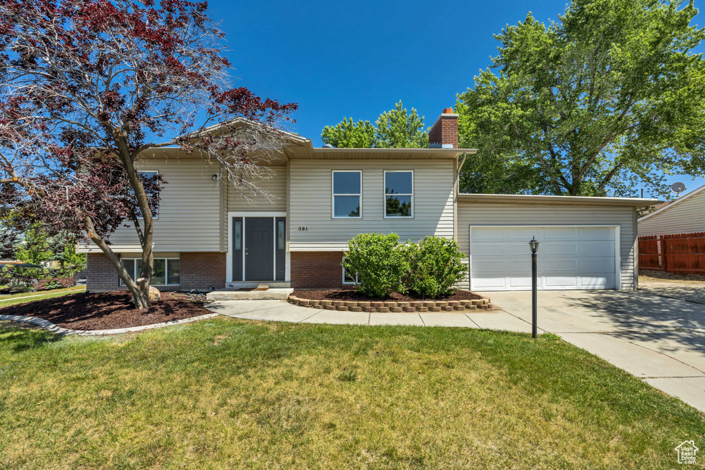 Split foyer home with driveway, an attached garage, and a chimney
