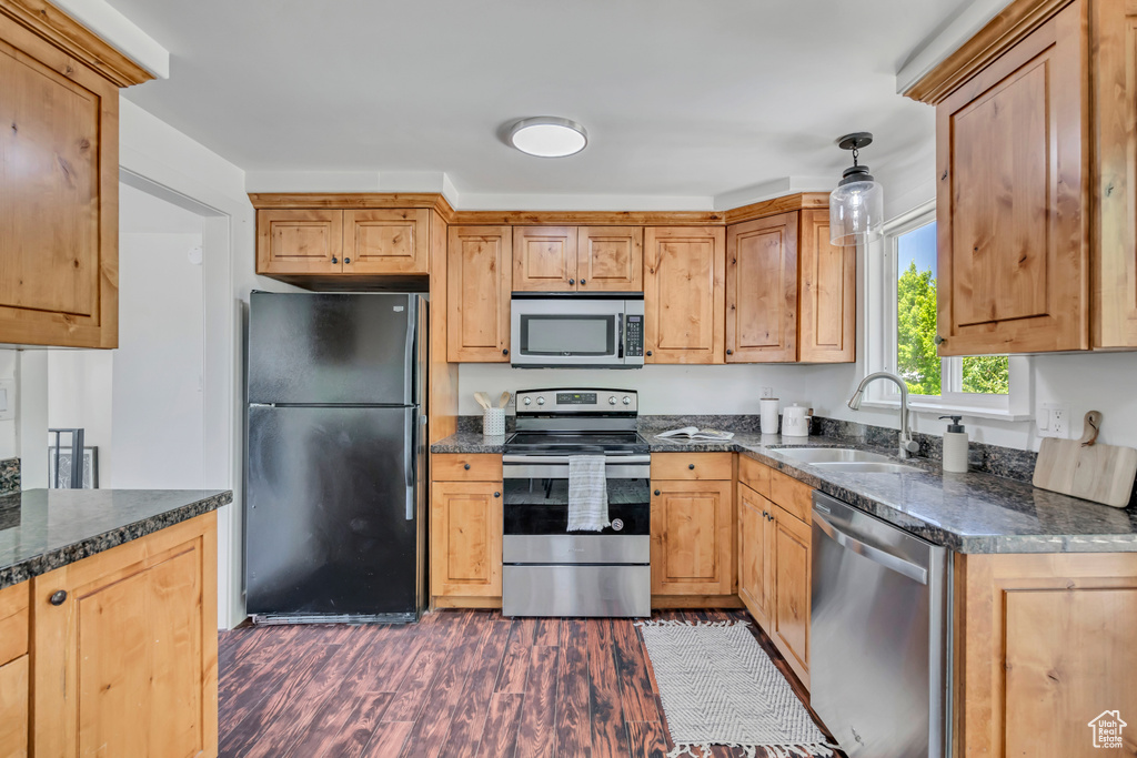Kitchen featuring appliances with stainless steel finishes, dark wood finished floors, dark stone countertops, and pendant lighting