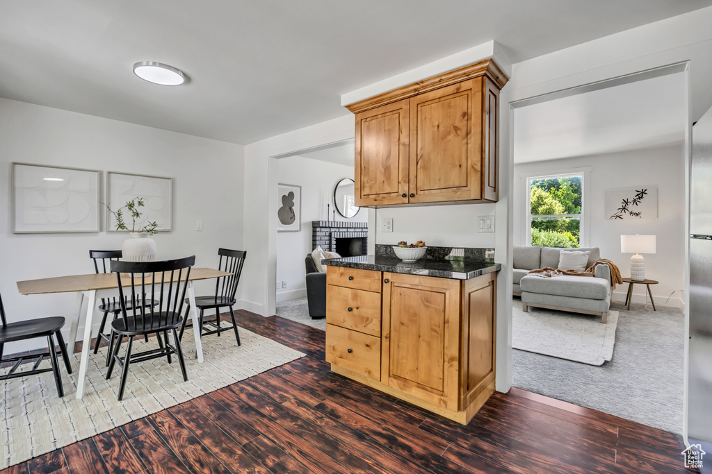 Kitchen with dark countertops, a brick fireplace, dark wood-style flooring, and brown cabinetry