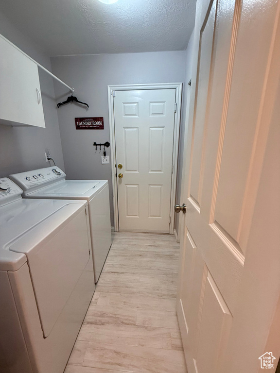 Laundry room with independent washer and dryer, cabinet space, light wood finished floors, and a textured ceiling