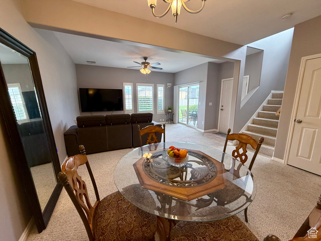 Dining space featuring light colored carpet, stairway, a ceiling fan, and a chandelier