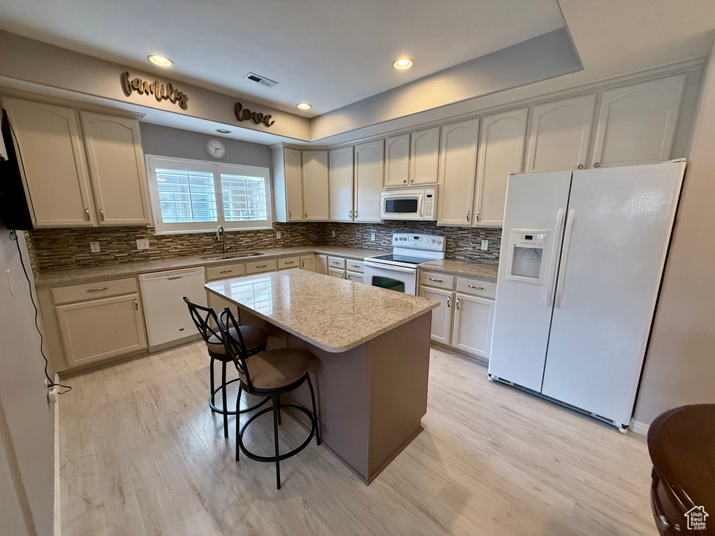 Kitchen with white appliances, light wood-style flooring, backsplash, a kitchen bar, and recessed lighting