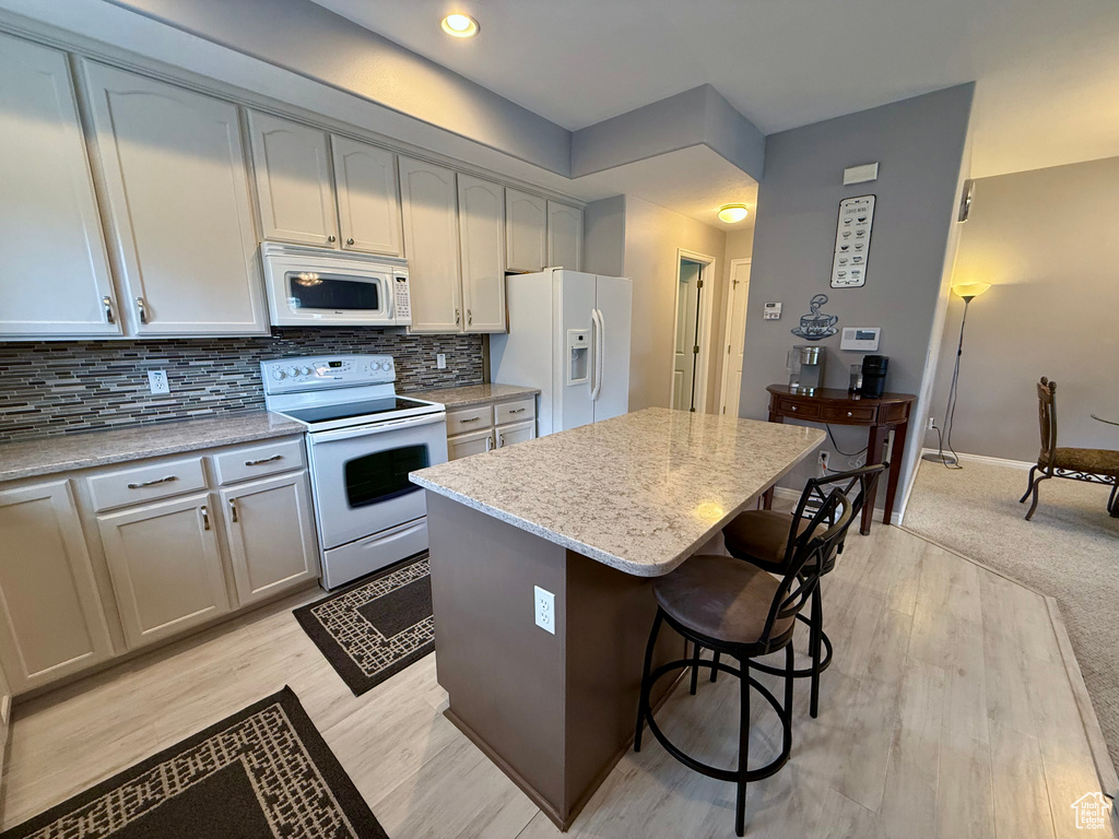 Kitchen featuring white appliances, a center island, a breakfast bar, tasteful backsplash, and light stone countertops