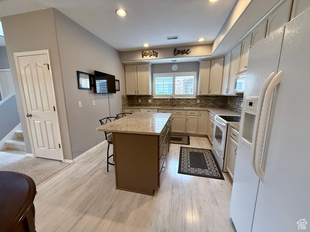 Kitchen featuring white appliances, a kitchen island, backsplash, a breakfast bar area, and light wood-style flooring