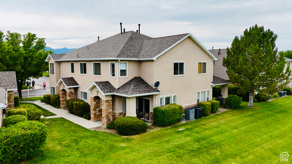 Rear view of house featuring stucco siding, a yard, a shingled roof, and stone siding