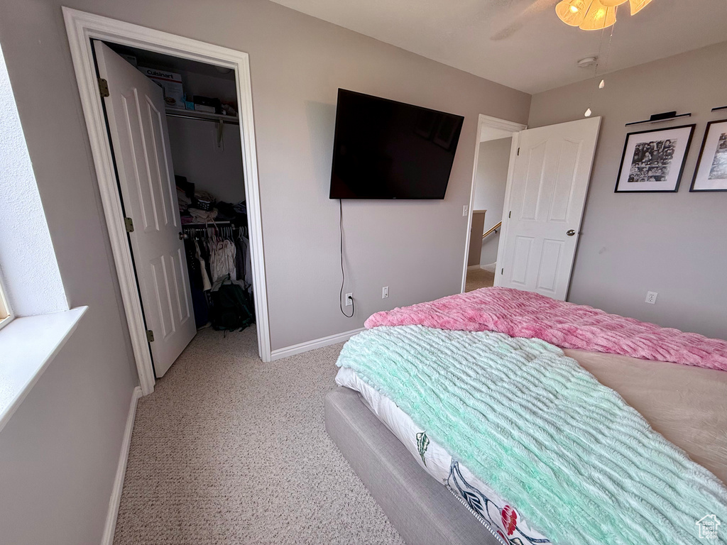 Bedroom with a walk in closet, light colored carpet, a closet, and a ceiling fan