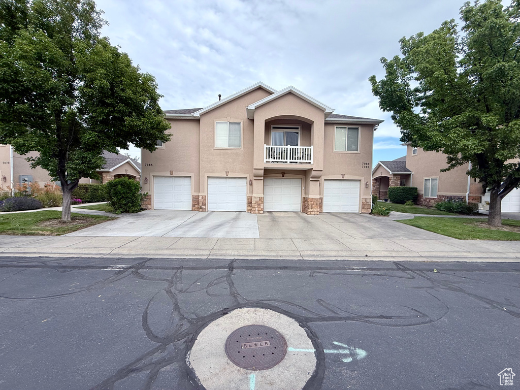 View of front of house with stucco siding, stone siding, an attached garage, driveway, and a balcony