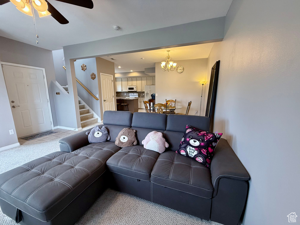 Living area with stairs, a ceiling fan, a chandelier, and light carpet
