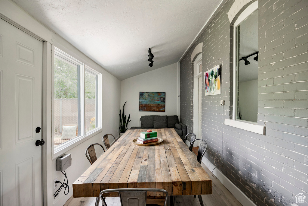 Dining area featuring wood finished floors, track lighting, lofted ceiling, and brick wall