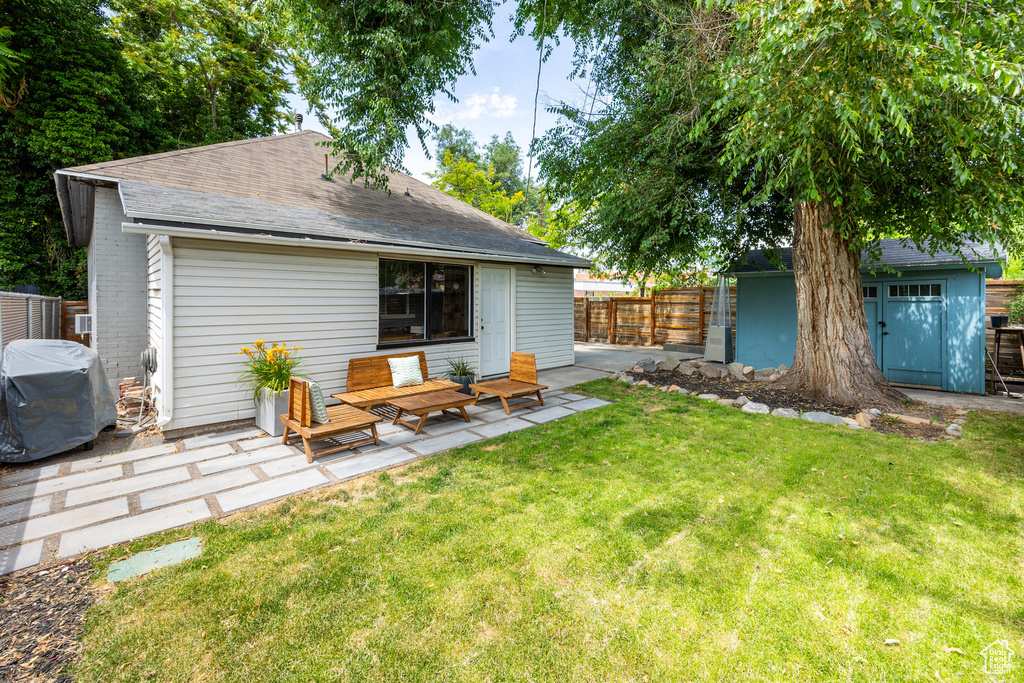 Rear view of property featuring a shingled roof, a patio area, and an outdoor structure
