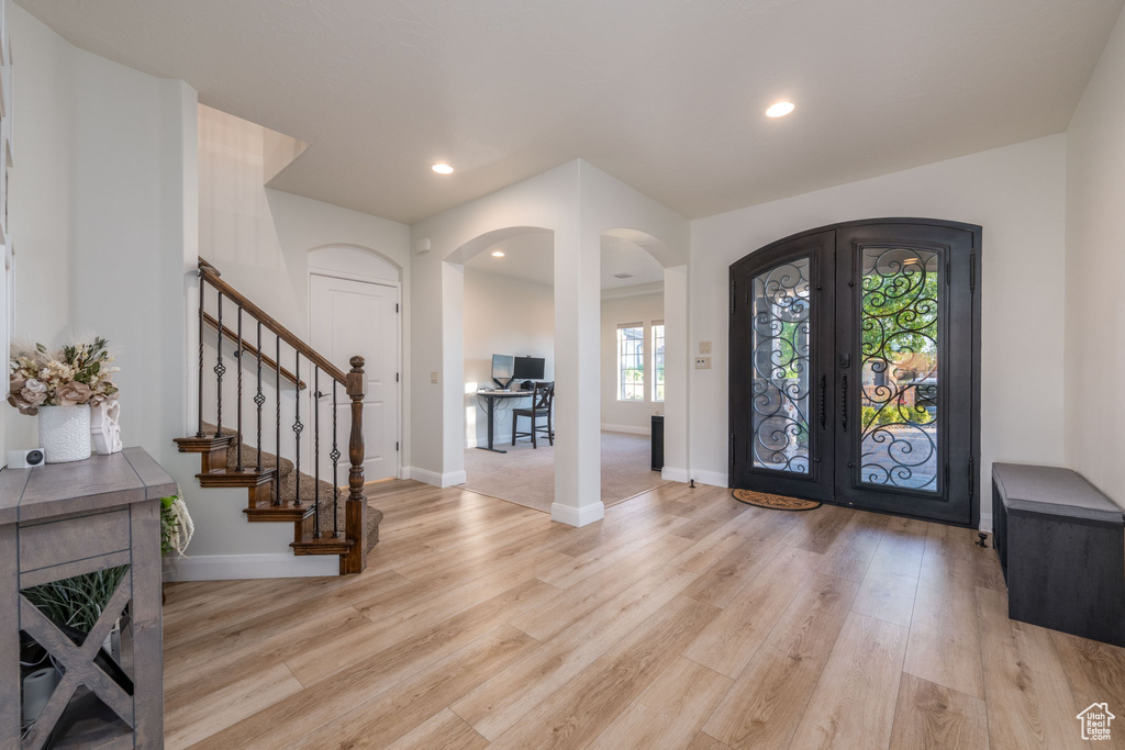 Foyer entrance featuring arched walkways, french doors, light wood finished floors, stairs, and recessed lighting