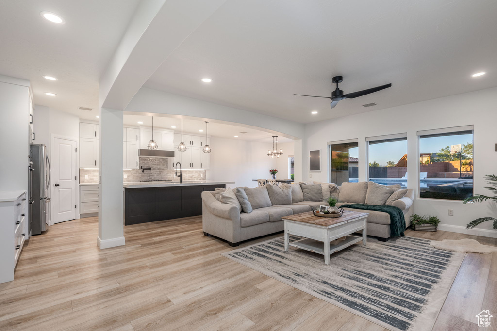 Living room with a ceiling fan, light wood-style flooring, recessed lighting, arched walkways, and a chandelier