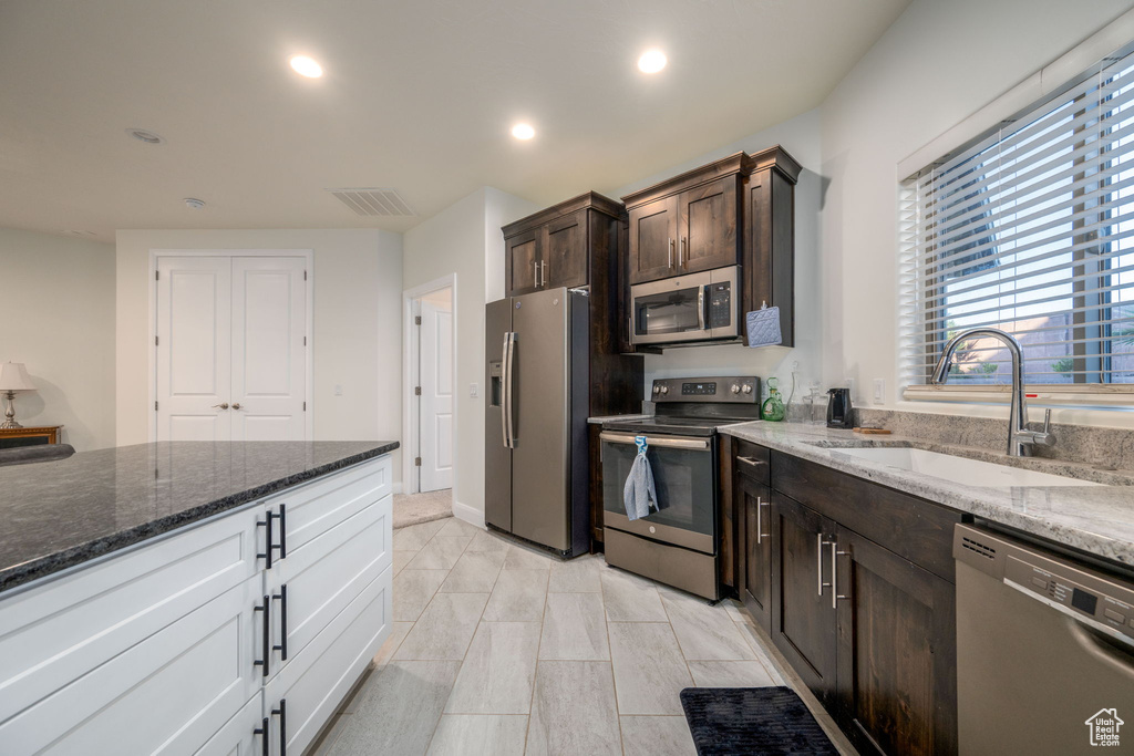 Kitchen with stainless steel appliances, dark brown cabinets, dark stone countertops, recessed lighting, and white cabinets