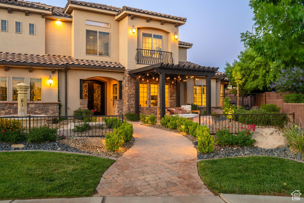 Mediterranean / spanish house with a tiled roof, a balcony, stucco siding, stone siding, and a pergola