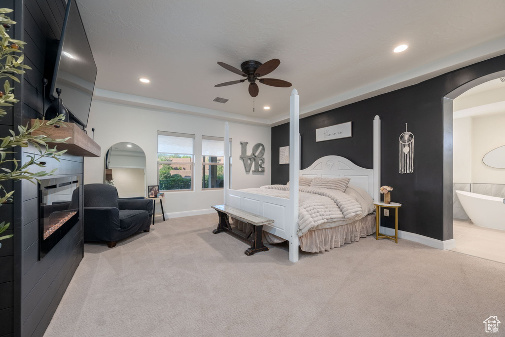 Bedroom with light carpet, recessed lighting, arched walkways, connected bathroom, and a ceiling fan