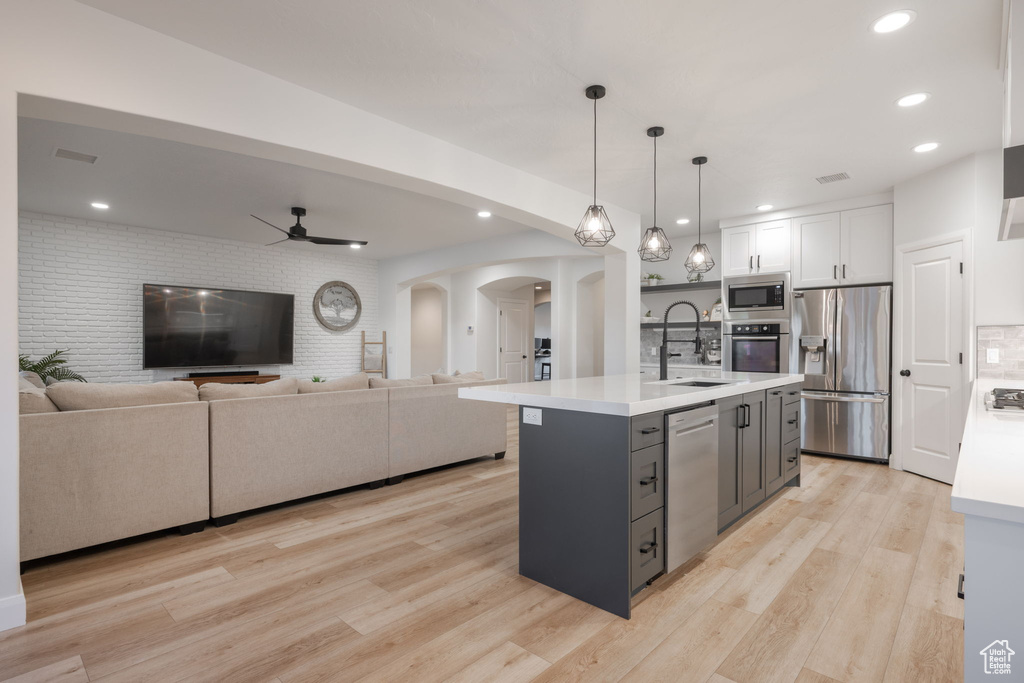 Kitchen with appliances with stainless steel finishes, arched walkways, light countertops, open floor plan, and white cabinetry