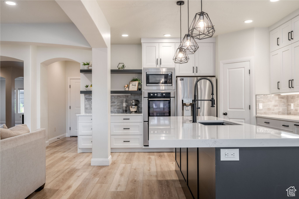 Kitchen with stainless steel appliances, arched walkways, open shelves, backsplash, and white cabinetry
