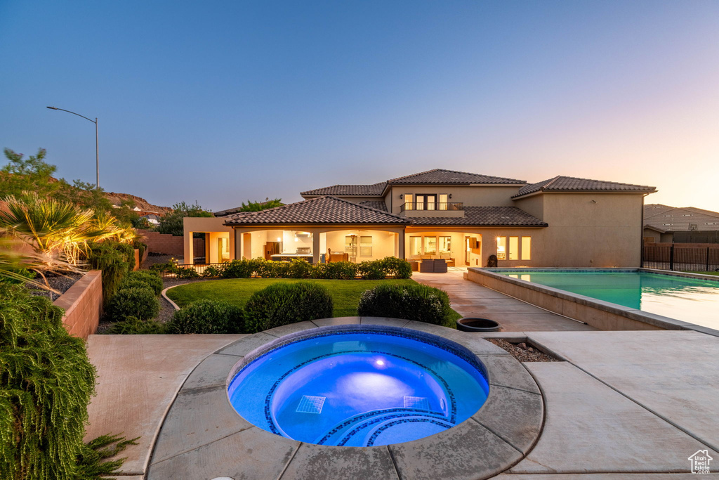 Back of house at dusk featuring an in-ground hot tub, an outdoor pool, a tile roof, stucco siding, and a patio