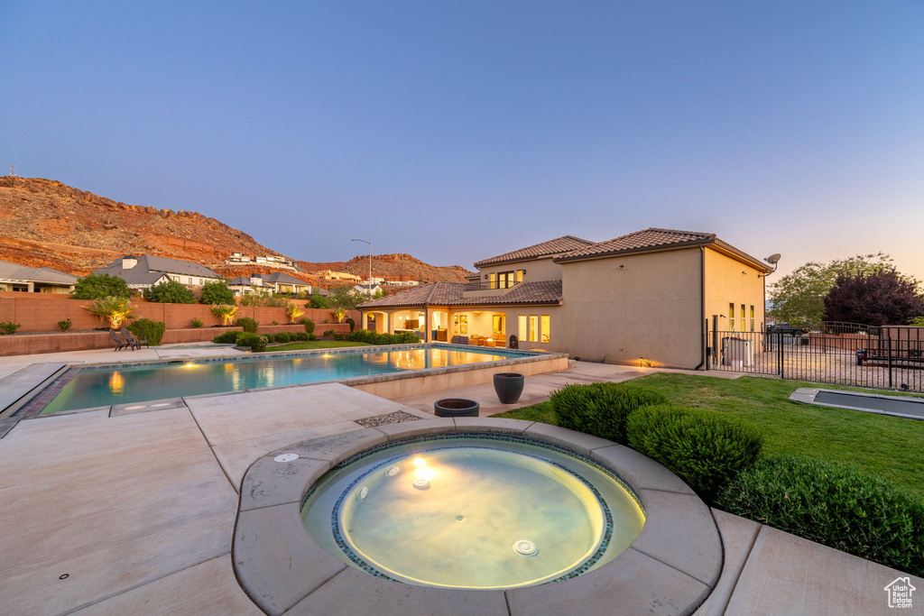 Pool at dusk with an in-ground hot tub, a fenced backyard, a patio, and a mountain view