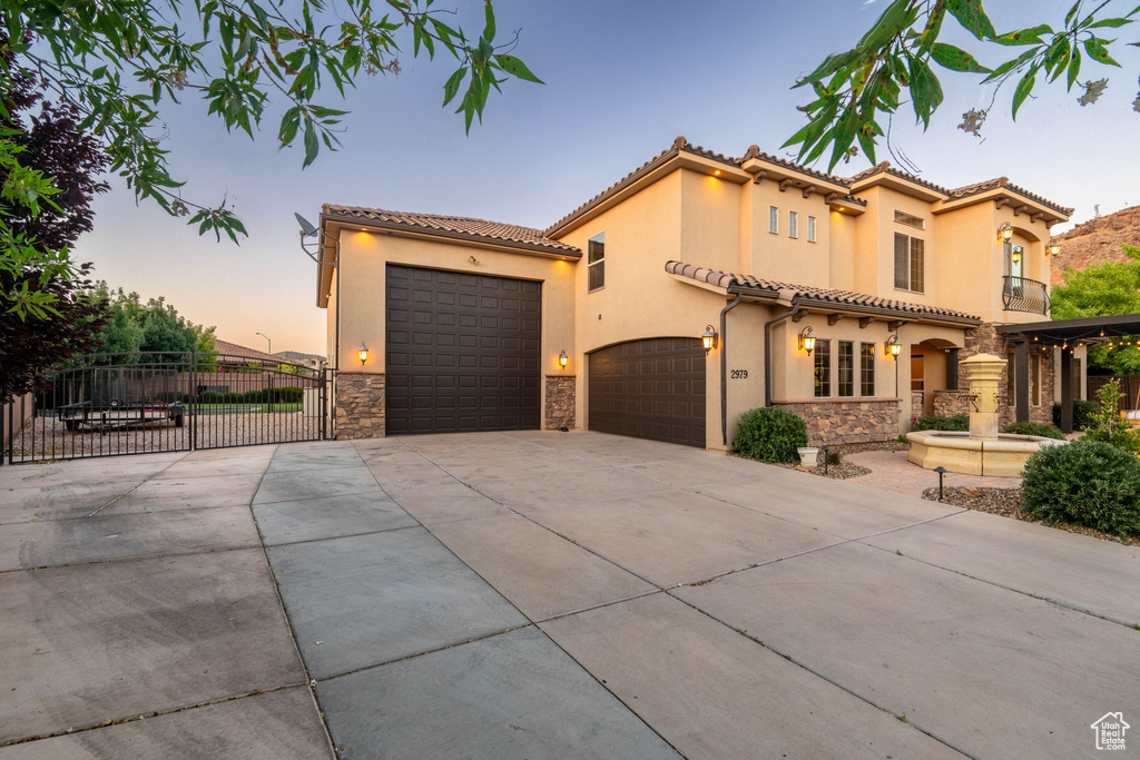 Mediterranean / spanish home with stone siding, concrete driveway, stucco siding, a gate, and a tiled roof