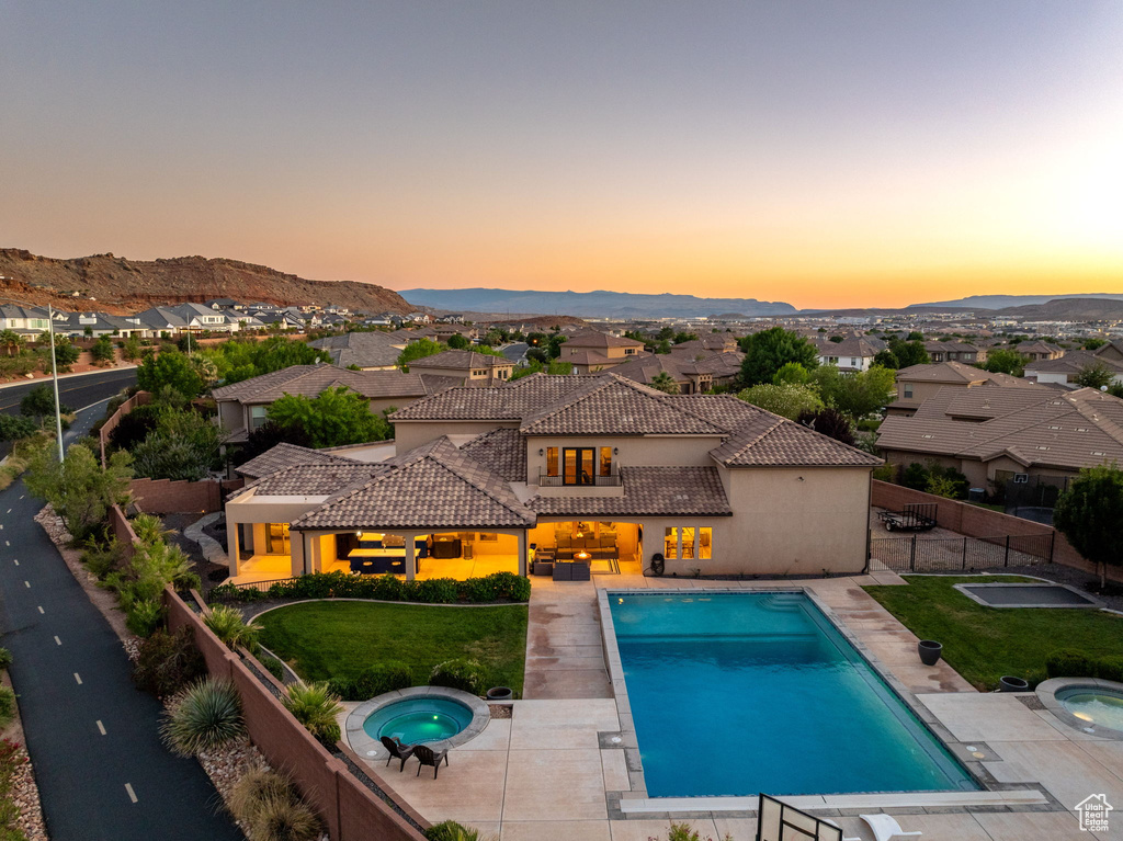 Pool at dusk featuring an in-ground hot tub, a fenced backyard, a residential view, a patio, and a mountain view