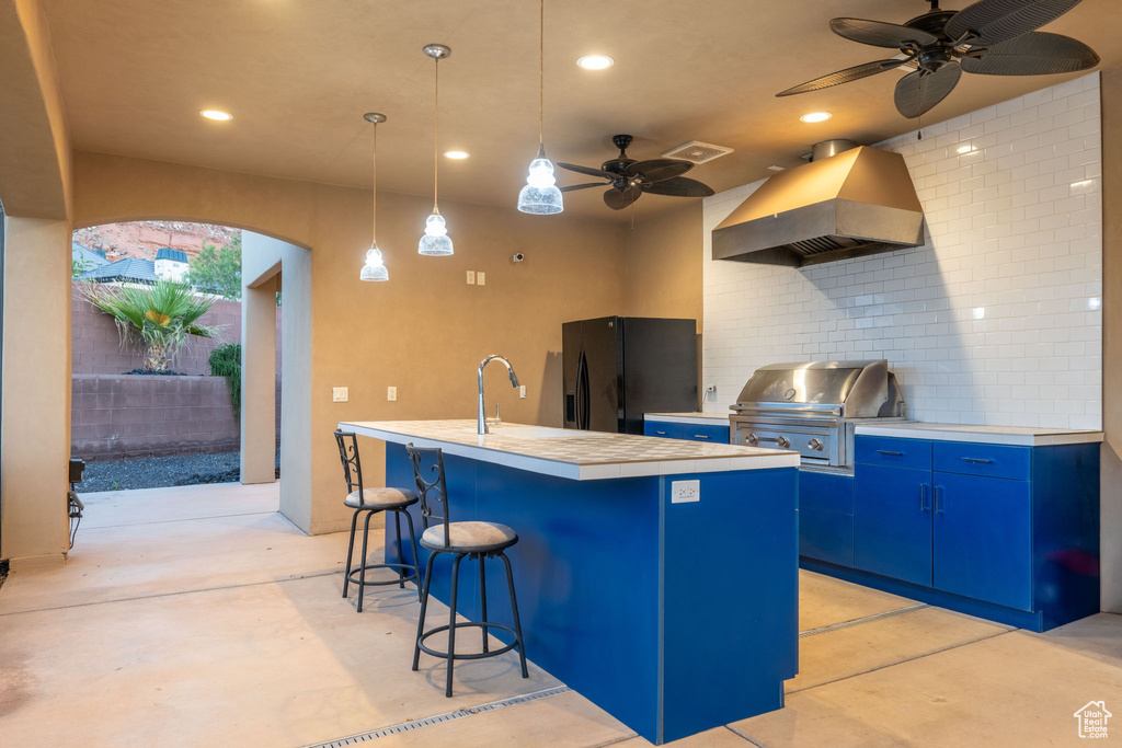 Kitchen featuring range hood, black fridge, blue cabinetry, unfinished concrete flooring, and recessed lighting