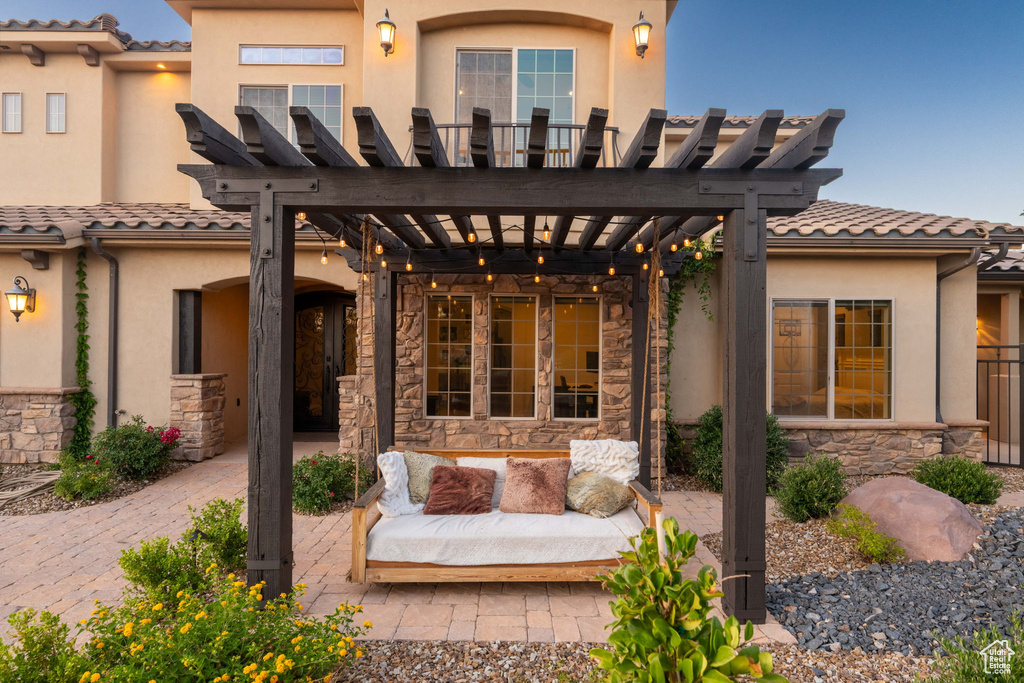 Rear view of house featuring a pergola, stone siding, stucco siding, a tiled roof, and a patio area