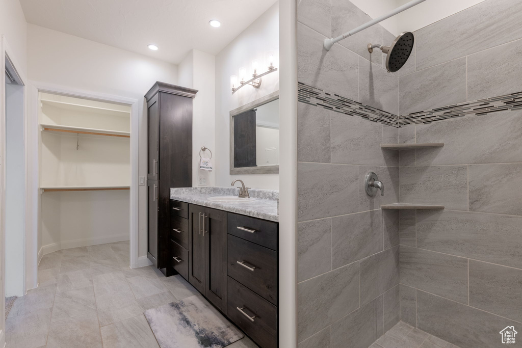 Bathroom featuring tiled shower, vanity, a spacious closet, and recessed lighting