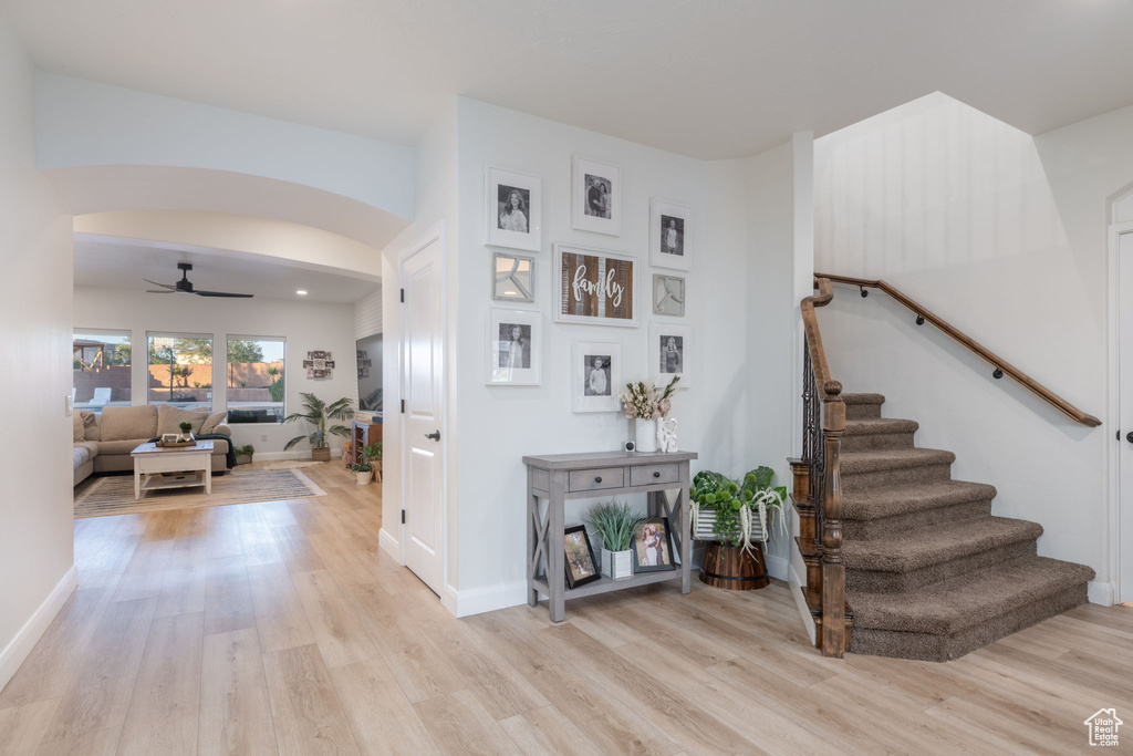 Foyer entrance featuring light wood-style floors, a ceiling fan, arched walkways, and stairs