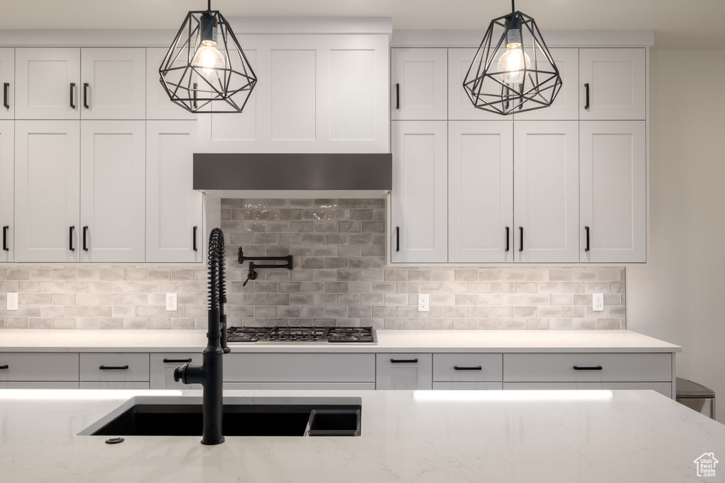 Kitchen featuring white cabinets, backsplash, light stone countertops, hanging light fixtures, and wall chimney exhaust hood