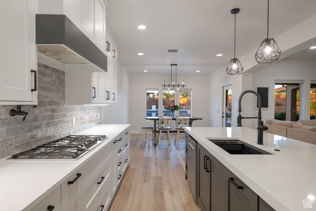 Kitchen featuring stainless steel appliances, wall chimney range hood, light wood finished floors, recessed lighting, and light stone countertops