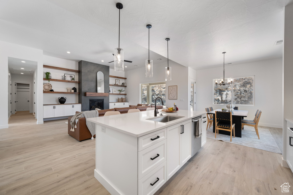 Kitchen with a fireplace, dishwasher, light wood finished floors, light countertops, and white cabinets