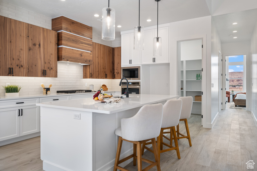 Kitchen with black microwave, decorative backsplash, light countertops, stainless steel oven, and an island with sink