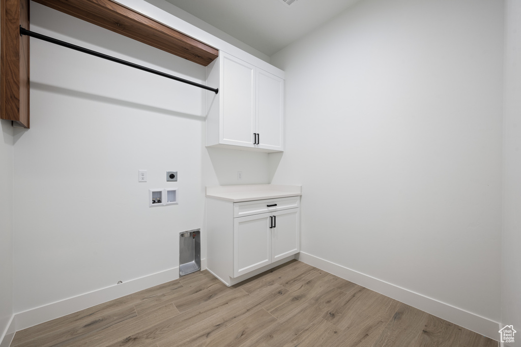 Washroom with hookup for an electric dryer, light wood finished floors, washer hookup, and cabinet space