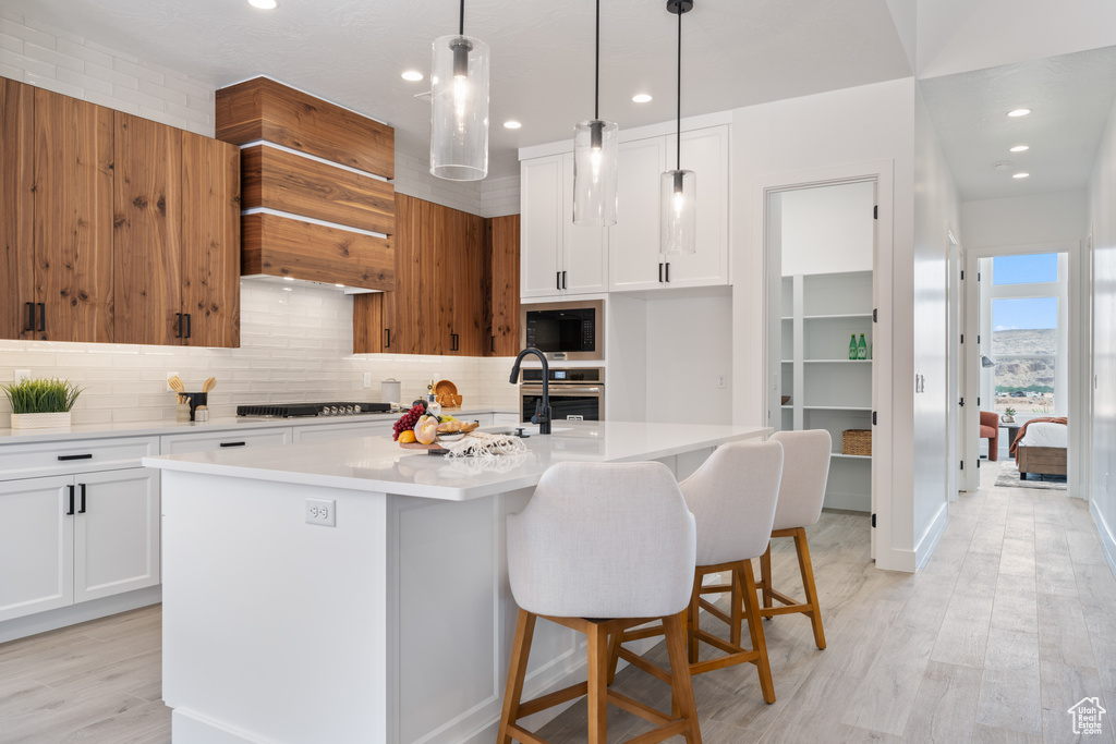 Kitchen with black microwave, light countertops, tasteful backsplash, stovetop, and a center island with sink