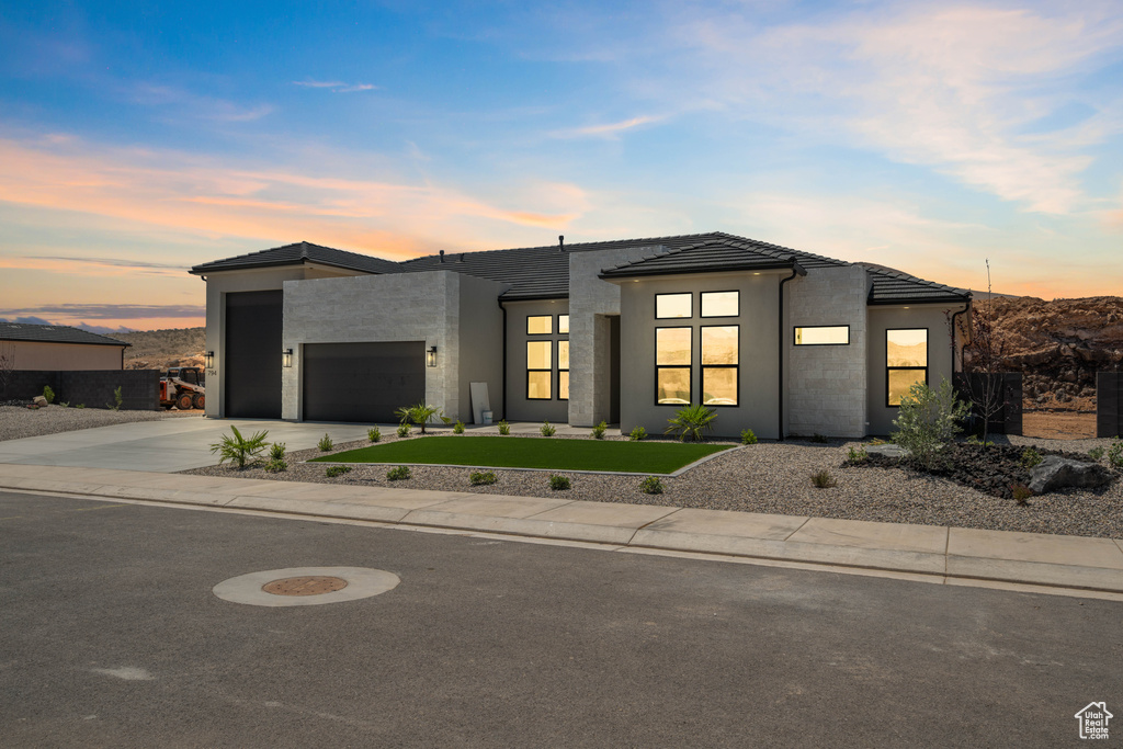 Contemporary house featuring a garage, driveway, a tiled roof, stucco siding, and a front yard