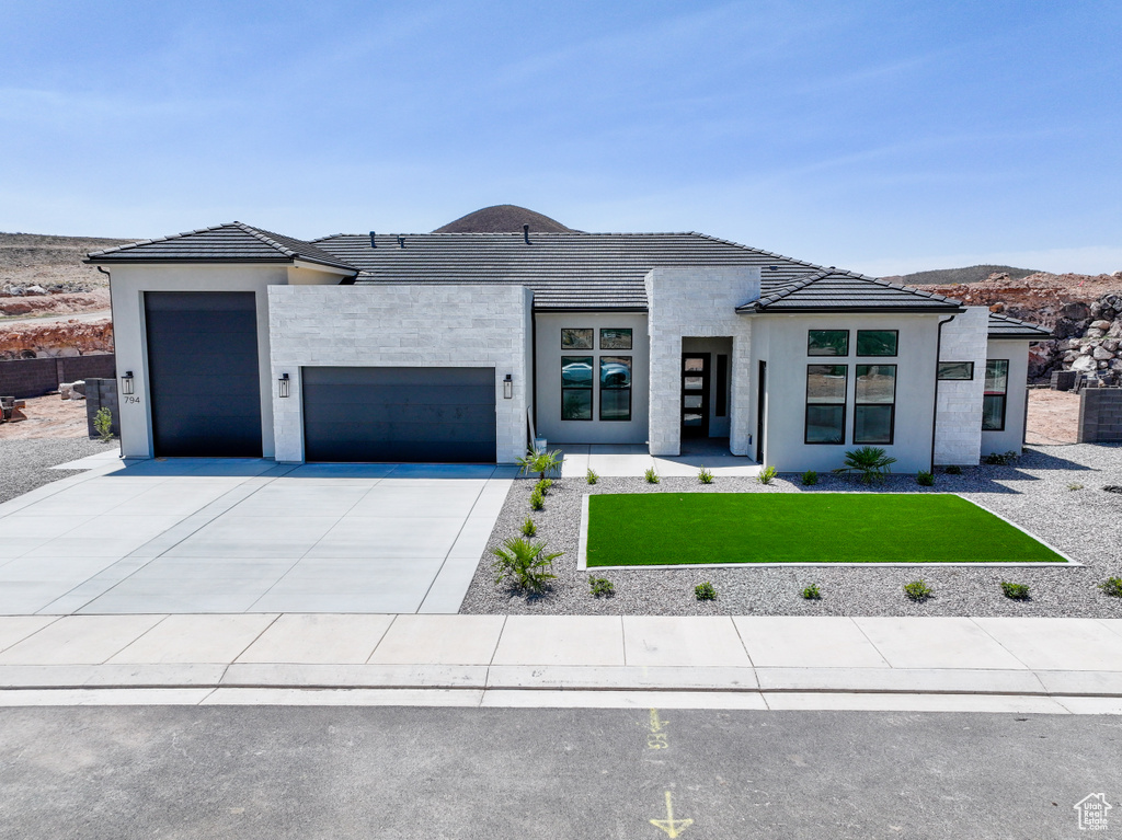 Contemporary home with a garage, a front yard, driveway, and stucco siding