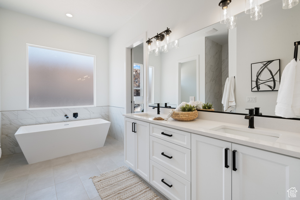 Full bath with tile walls, double vanity, a freestanding bath, tile patterned flooring, and a wainscoted wall