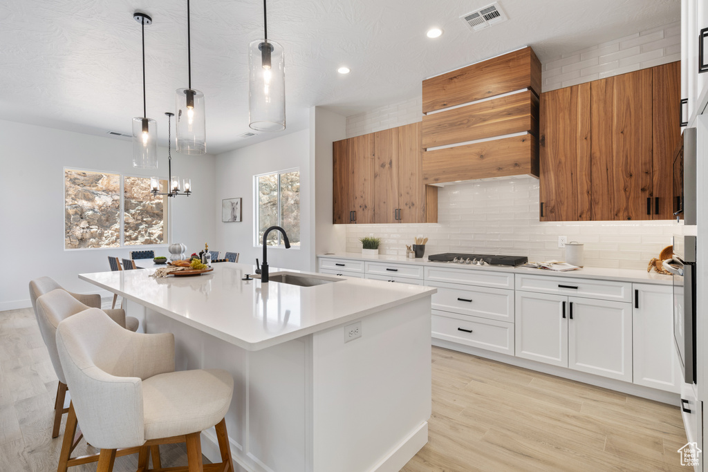Kitchen featuring stainless steel appliances, tasteful backsplash, light countertops, an island with sink, and white cabinetry