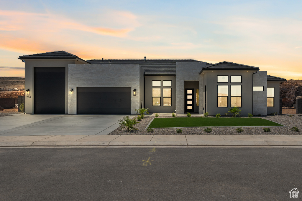 Contemporary house featuring a garage, a front lawn, concrete driveway, stucco siding, and a tiled roof