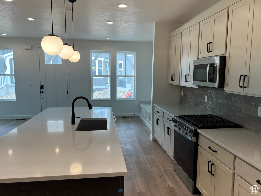 Kitchen with stainless steel microwave, gas range, light wood-style flooring, light countertops, and a textured ceiling