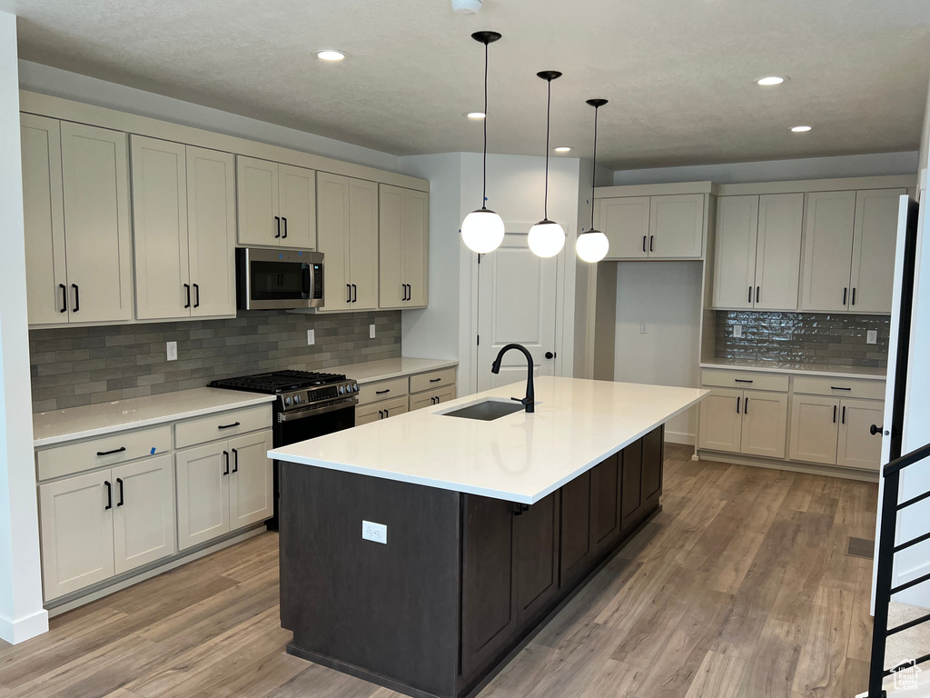 Kitchen featuring stainless steel microwave, light wood-style flooring, tasteful backsplash, light countertops, and a kitchen island with sink