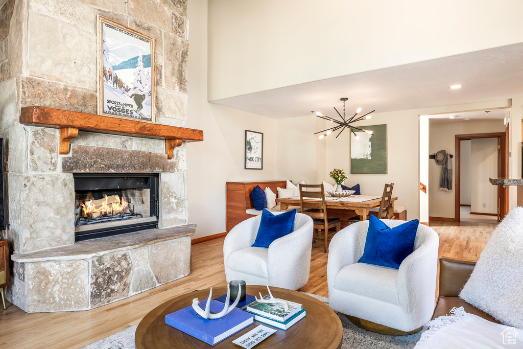 Living area with a stone fireplace, a chandelier, wood finished floors, and a high ceiling