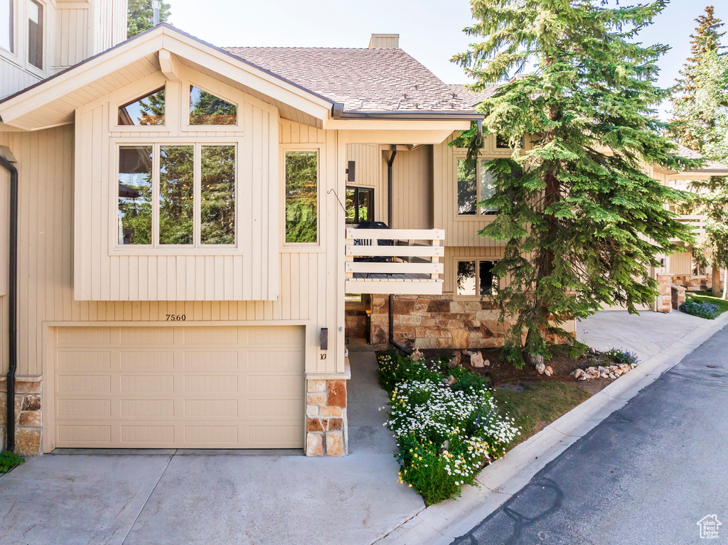 View of front of property featuring stone siding, an attached garage, concrete driveway, and roof with shingles