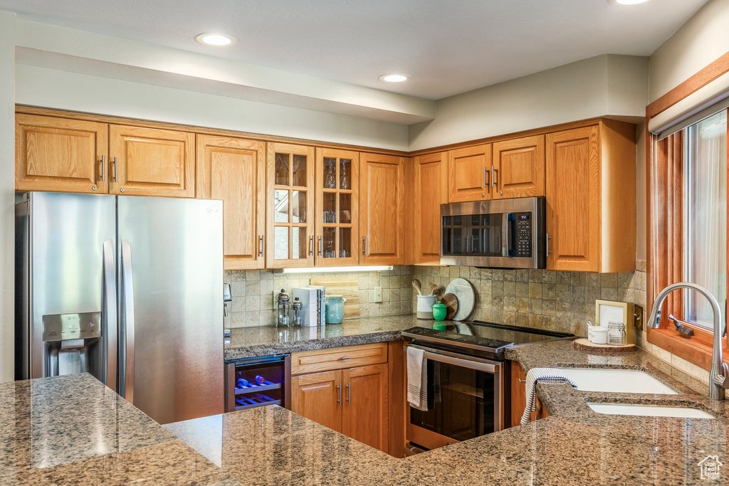 Kitchen with stainless steel appliances, glass insert cabinets, tasteful backsplash, recessed lighting, and beverage cooler